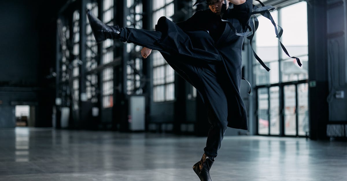 Martial artist in black attire executes powerful jump kick in spacious industrial setting.